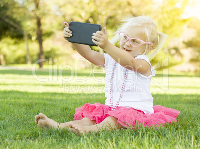 Little Girl In Grass Taking Selfie With Cell Phone