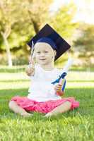 Little Girl In Grass Wearing Graduation Cap Holding Diploma With