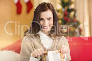 Brunette opening a gift on the couch at christmas