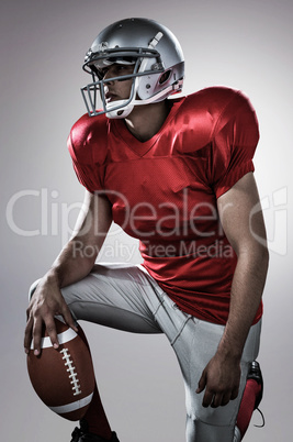 Composite image of sportsman holding american football while kne