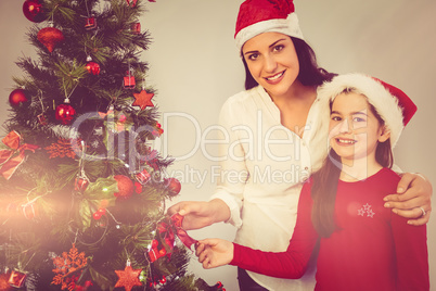 Mother and daughter hanging christmas decorations on tree