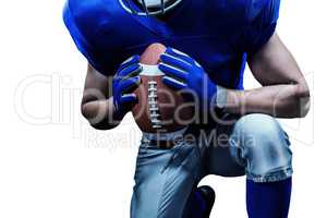 Mid section of American football player kneeling while holding b