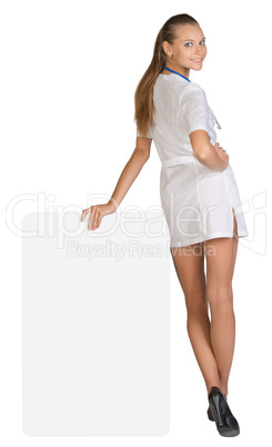 Young woman doctor standing backward, leaning hand on an empty billboard