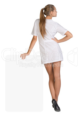 Young woman doctor standing backward, leaning hand on an empty billboard