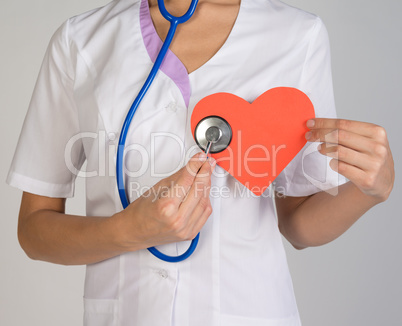 Doctor with stethoscope examines red paper heart