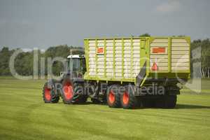 Transport of cut grass with green tractor and grass trailer.