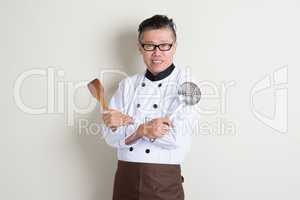Mature Asian Chinese chef holding kitchen tools