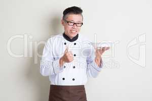 Mature Asian Chinese chef presenting dish and thumb up