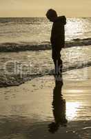 Silhouette and reflection of a little boy on the beach.