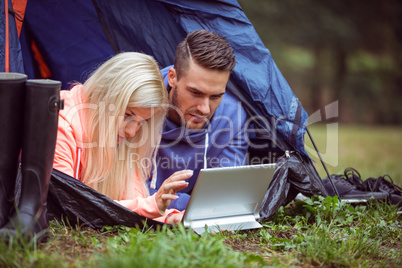 Happy couple lying in their tent using tablet