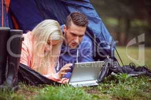 Happy couple lying in their tent using tablet