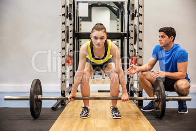 Woman lifting barbell with trainer spotting her