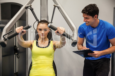Confident woman using weights machine with trainer