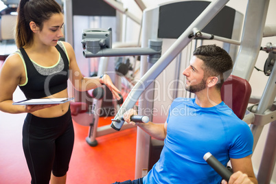 Trainer working with athlete at weights machine