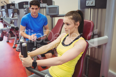 Fit woman using weights machine with trainer