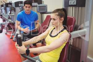 Fit woman using weights machine with trainer