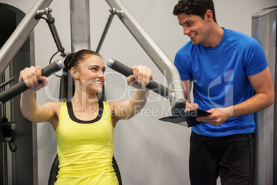 Confident woman using weights machine with trainer