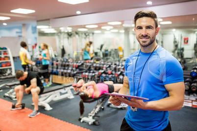 Handsome trainer using tablet in weights room