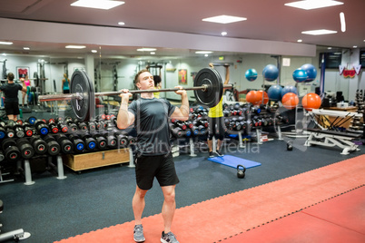 Fit man lifting heavy barbell in weights room