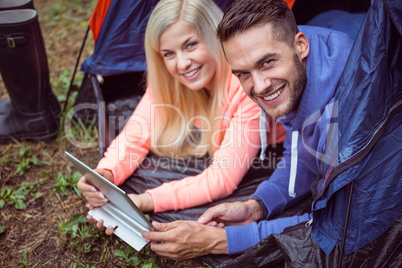 Happy couple lying in tent using tablet