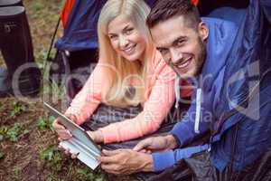 Happy couple lying in tent using tablet