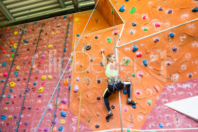 Fit blonde rock climbing indoors