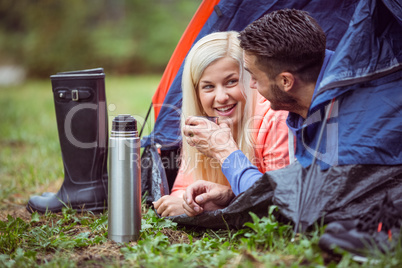 Happy couple lying in tent having hot drinks