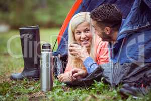 Happy couple lying in tent having hot drinks