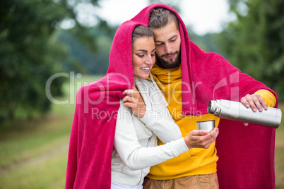 Happy couple under a blanket pouring hot drink