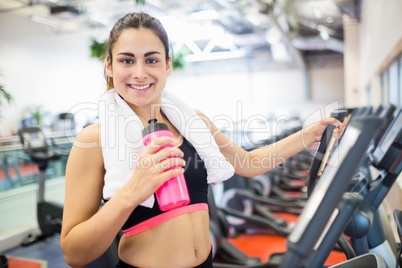 Smiling woman drinking on the cross trainer