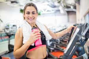 Smiling woman drinking on the cross trainer