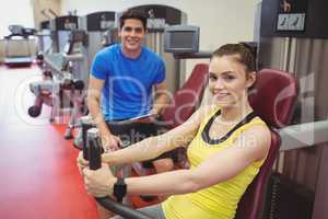 Fit woman using weights machine with trainer