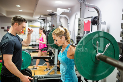 Fit woman lifting heavy barbell in weights room