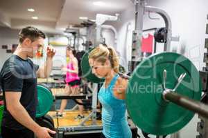 Fit woman lifting heavy barbell in weights room