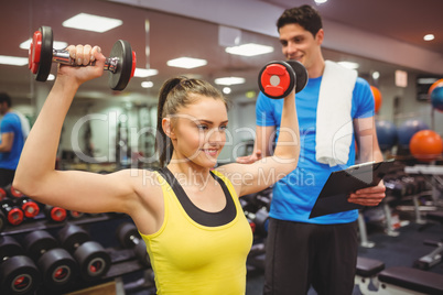 Woman lifting dumbbells with her trainer