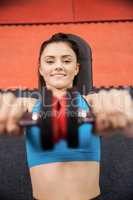 Focused woman lifting dumbbells while lying down