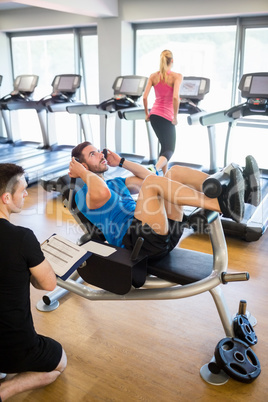 Fit man doing sit ups with trainer