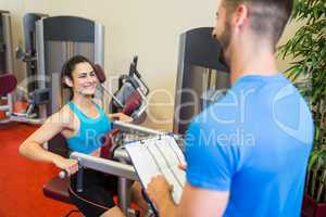 Smiling woman on weights machine beside trainer
