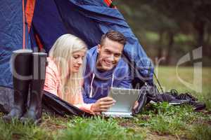 Happy couple lying in their tent using tablet
