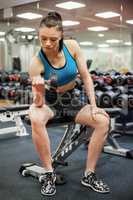 Focused woman lifting dumbbell while sitting down