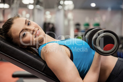 Smiling woman lifting dumbbell while lying down