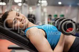 Smiling woman lifting dumbbell while lying down