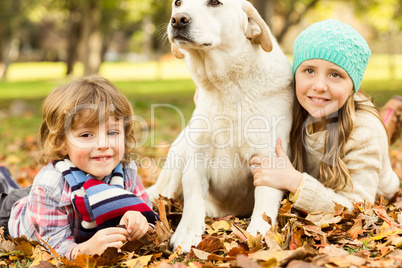 Young boy and girl lying with their dog in leaves