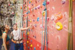Instructor showing woman rock climbing wall
