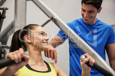 Confident woman using weights machine with trainer
