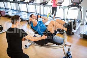 Fit man doing sit ups with trainer