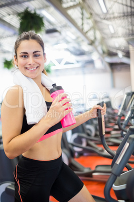 Smiling woman drinking on the cross trainer