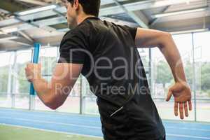 Fit man running on track with baton