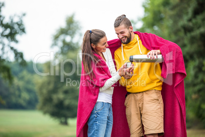 Happy couple under blanket pouring hot drink