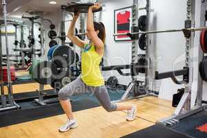 Determined woman doing lunges while holding a weight overhead